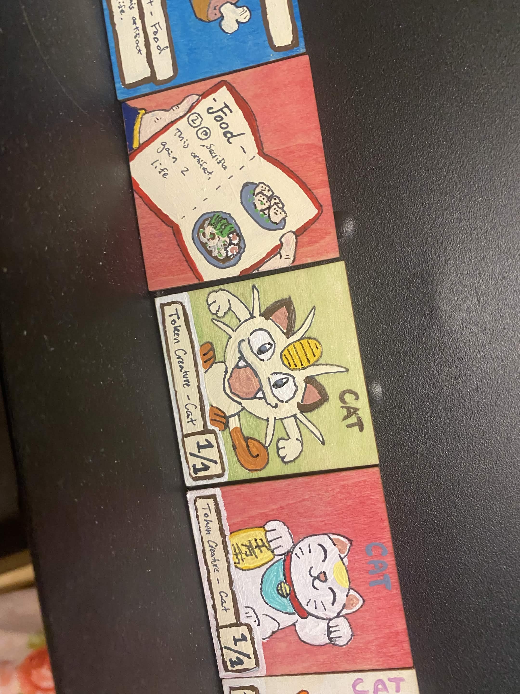 wooden squares showing a menu, meowth (pokemon), and a lucky cat. Text is the same as a Magic the Gathering food and cat tokens