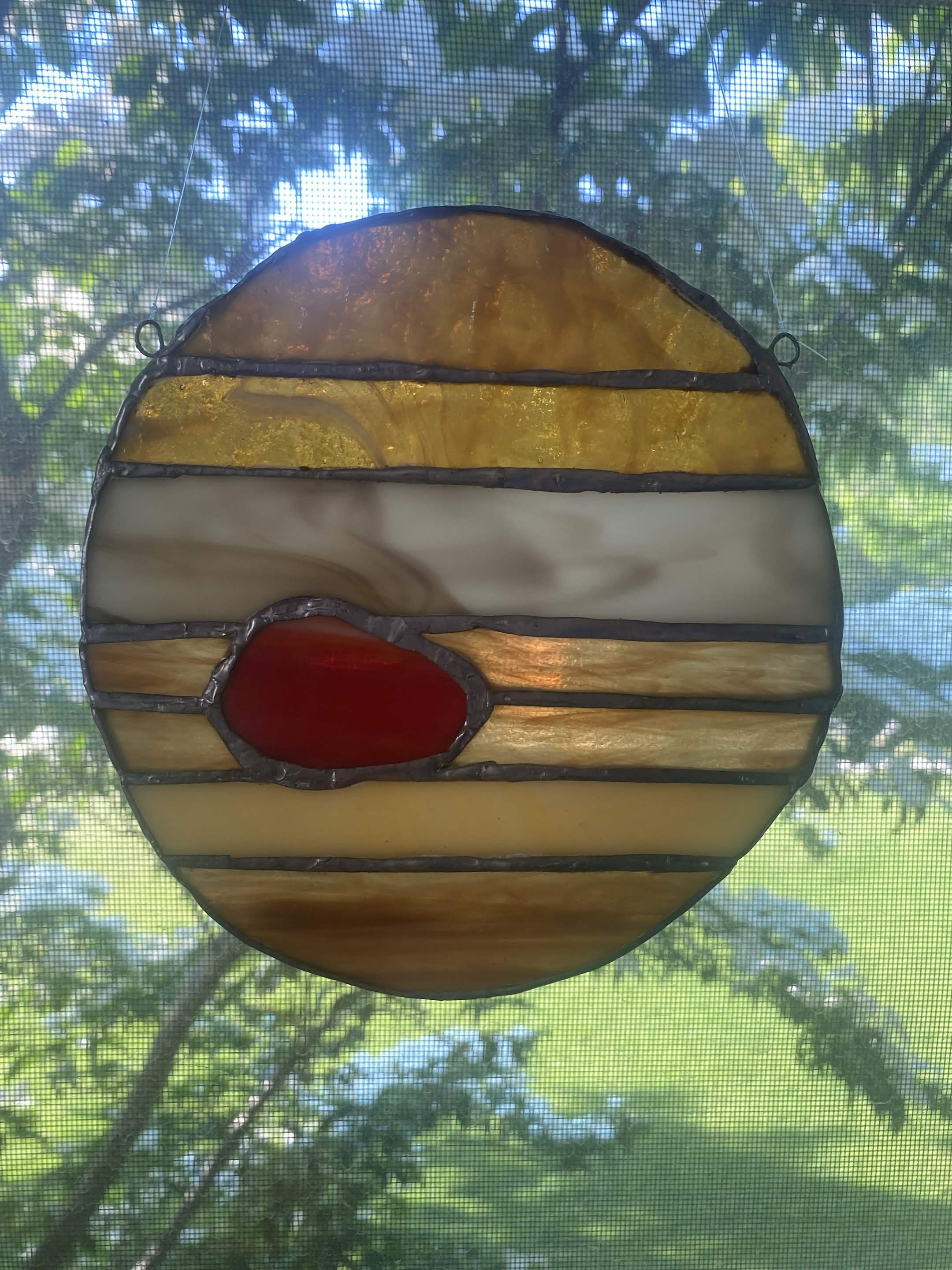 Jupiter suncatcher on window in front of tree.