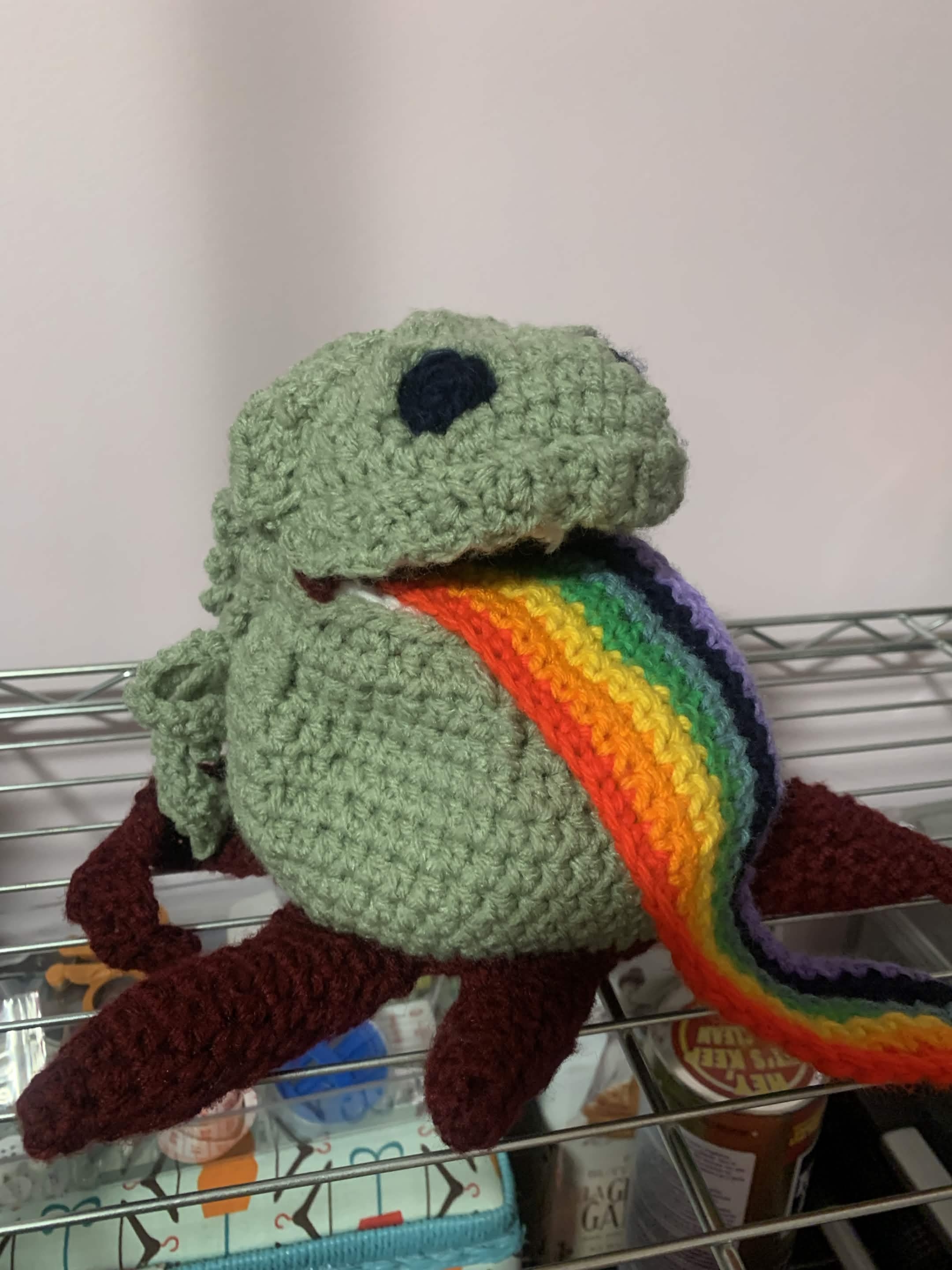 Small green tentacle'd creature vomiting up rainbows, in crochet