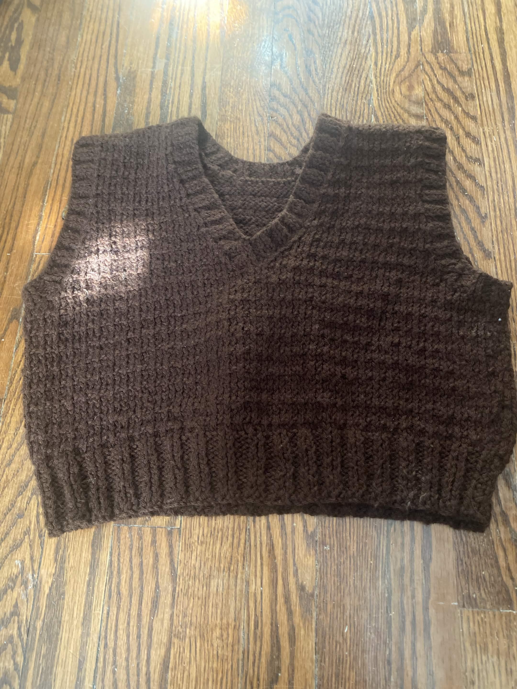 dark brown solid knit sweater vest. sleves are ribbed and bodice is majority stockinette, but with some slight texture to it
