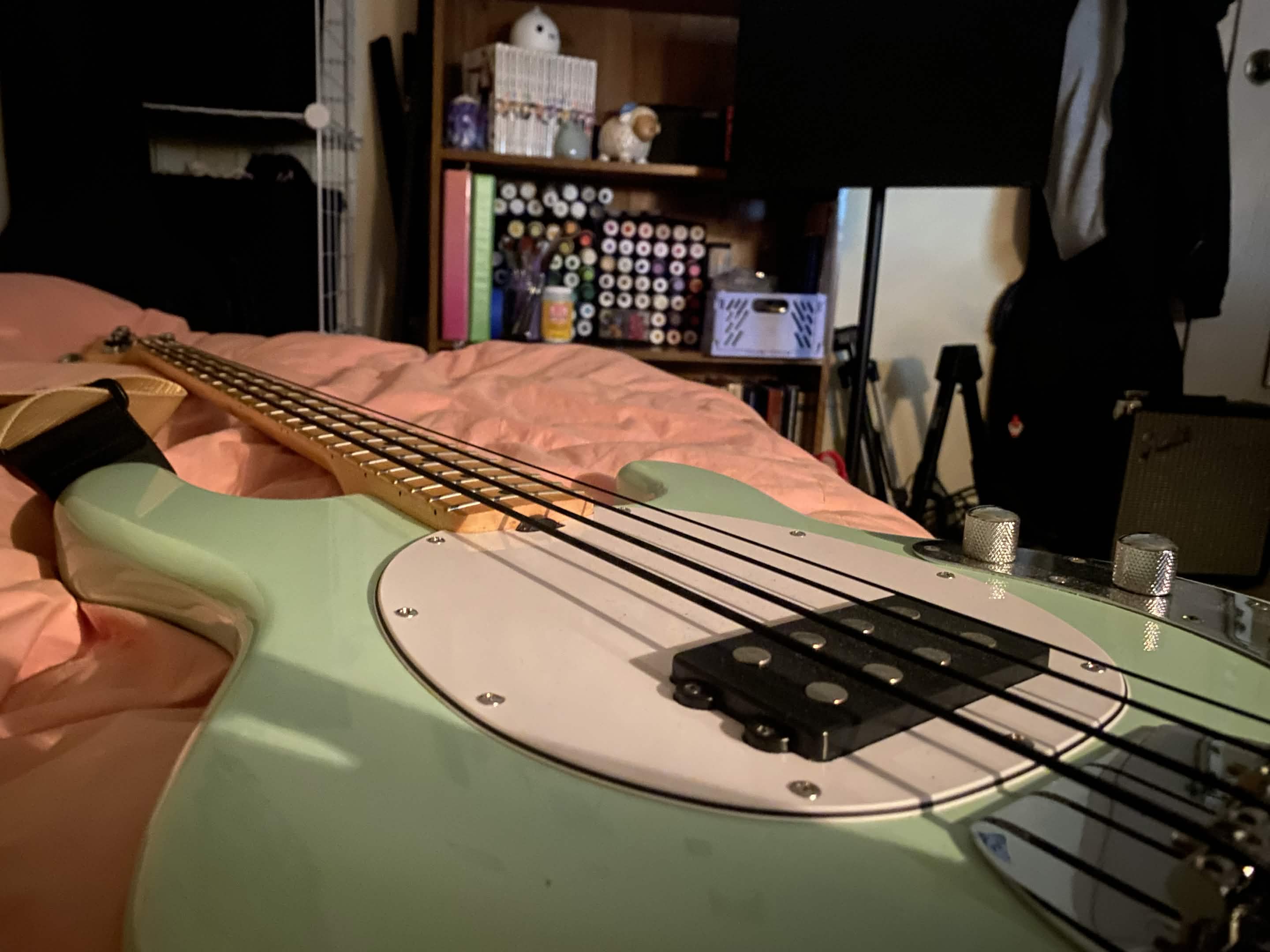 light blue bass guitar lies on dusty rose comforter